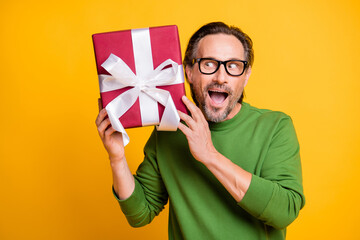 Photo portrait of man in glasses looking interested on gift box wrapped with ribbon isolated...