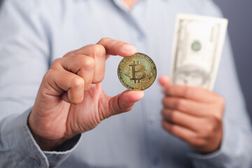 Investor guy showing a bitcoin golden coin and US banknotes while standing in the studio. Close-up photo. Space for text. Virtual cryptocurrency and future money concept
