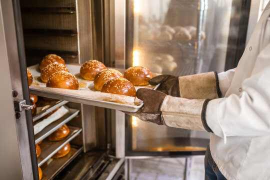 Male hands in gloves getting buns from oven - Powered by Adobe
