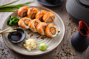 Baked sushi maki rolls with salmon, crab and spicy sauce on a plate with chopsticks, soy sauce, wasabi and ginger. Japanese traditional fish food closeup served for lunch in modern gourmet restaurant