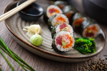 Sushi maki rolls with tuna, flying fish caviar, crab, avocado on a plate with chopsticks, soy sauce, wasabi and ginger. Japanese traditional food closeup served for lunch in modern gourmet restaurant