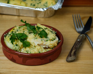 Delicious Hake served on a green sauce with parsley leaves in a clay bowl with cutlery
