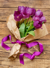 Purple tulips bouquet with purple ribbon on wooden table