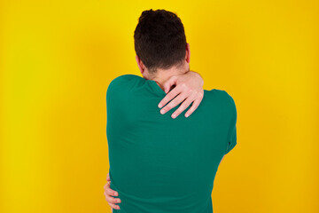 young Caucasian man wearing green T-shirt against yellow wall hugging happy and positive from...