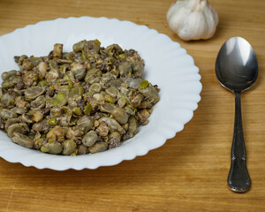 Habas a la Catalana, Tasty stew of beans in a white dish with a metal spoon and garlic gloves