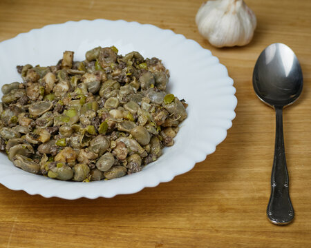 Habas a la Catalana, Tasty stew of beans in a white dish with a metal spoon and garlic gloves