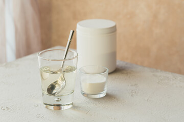 Glass with collagen dissolved in water and collagen protein powder on a light beige table