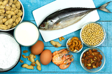Major food allergens include milk, egg, penuts, fish, shrimp, wheat flour, soya, almond and cashew nut on blue rustic wooden table, top view. Allergy food concept.