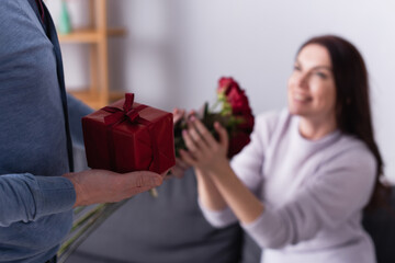 Man holding gift box near wife with flowers on blurred background