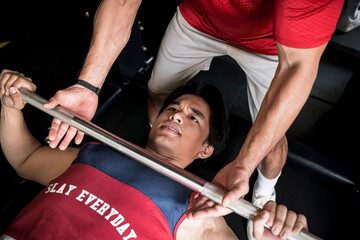 A young asian man gets a spot or assist from his personal trainer while doing bench presses.