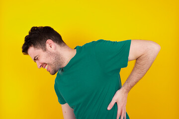 young Caucasian man wearing green T-shirt against yellow wall Suffering of backache, touching back with hand, muscular pain