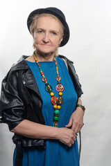 Elegant woman aged, in a black hat, fashionable leather jacket with a bag.older model posing in studio.