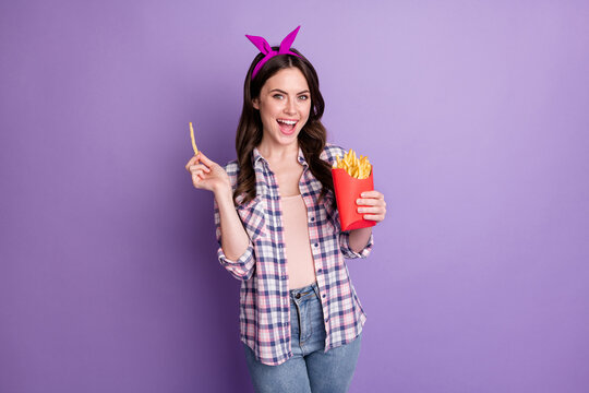 Photo portrait of nice girl eating french fries crispy chips wearing headband checkered shirt isolated on vivid purple color background