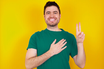 young handsome caucasian man wearing green t-shirt against yellow background smiling swearing with...