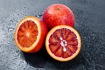 Bloody oranges whole and cut in half on black slate board with water drops. Red sicilian orange...