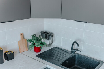 On the kitchen countertop are a chopping board, black containers, and a flower in a red board, next to the sink. The concept of minimalism and environmental friendliness in the kitchen