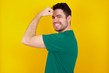 Portrait of powerful cheerful young handsome caucasian man wearing green t-shirt against yellow...