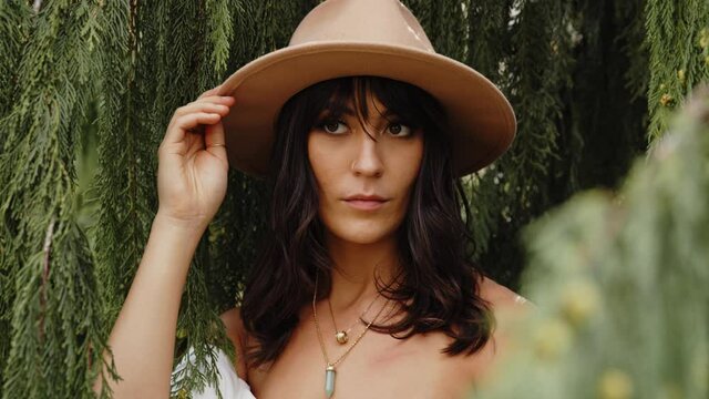 Brunette model woman posing in wide brim fedora by pine tree, Slowmo Closeup