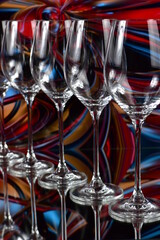 Diagonal of five empty wine glasses on a colored abstract background and reflective surface