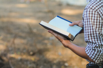 A young man holding a Bible opened for learning to understand the Bible in order to pray to God and to ask God to protect himself and his family. The concept of Bible learning and faith in God