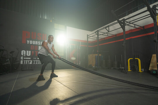 Black African American man doing battle ropes for cardio. Muscle strength training workout at gym fitness center club. Exercise indoor with sport equipment. Athletic. People lifestyle.