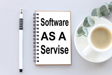 Software as a service. text on white notepad paper. near cups with coffee and plants on a gray background.