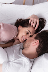 Obraz na płótnie Canvas Smiling woman in pajama lying near husband on white bedding