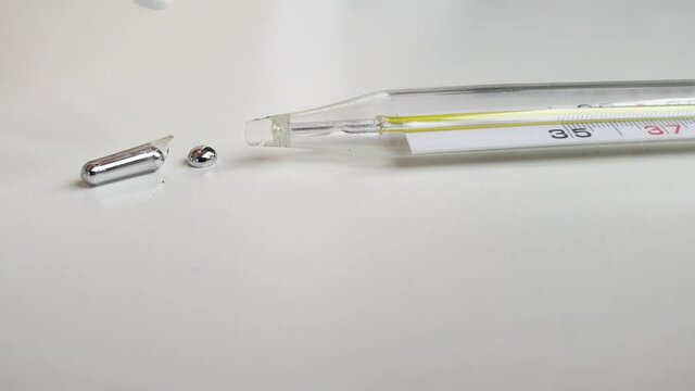 Mercury thermometer broken, close-up on white background. Remove mercury from  table  surface, combining small metal balls