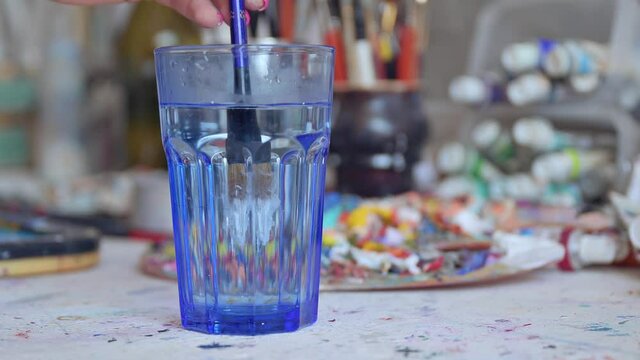 Artist dabs a brush in a glass with water using watercolor paint