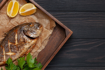 Baked dorado fish with lemon and parsley in a dish on the table. Top View