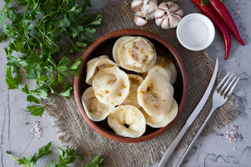 Vegan dumplings with pumpkin and fresh herbs in a clay bowl on a gray background. Top view