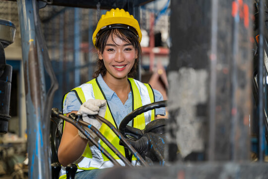 A female engineer is controlling a forklift in a spare parts factory. A smiling woman is deliberately practicing machine control in a factory in Industrial Engineering worker concept.