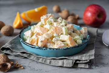 Vegetarian food: salad with orange, celery and apple in a beautiful plate on a gray background