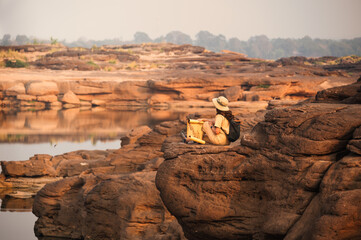 Asian woman explorer sitting on rock cliff with looking at paper map in Sam Phan Bok grand canyon