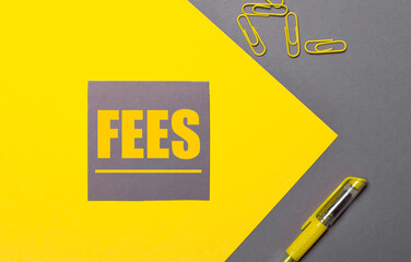 On a gray and yellow background, a gray sticker with yellow text FEES, yellow paper clips and a...