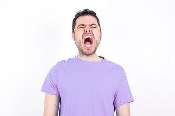 Obraz premium Stressful young handsome caucasian man wearing purple t-shirt against white background screams in panic, closes eyes in terror, keeps hands on head, finds out terrified news, can't believe it.