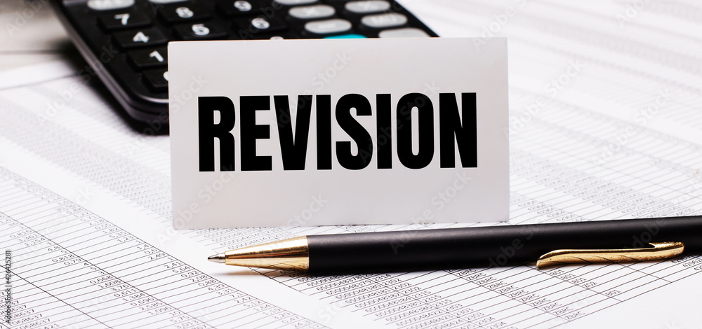 Poster on the table there are reports, a pen, a calculator and a white card with the text revision. defocus