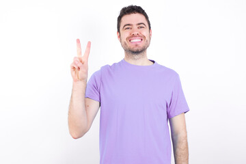 young handsome caucasian man wearing purple t-shirt against white background showing and pointing up with fingers number two while smiling confident and happy.