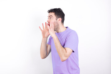young handsome caucasian man wearing purple t-shirt against white background with shocked facial...