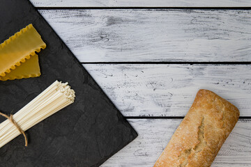 Bread, bun, focaccia, ciabatta, udon, pasta, flour products on a wooden background. Mediterranean...