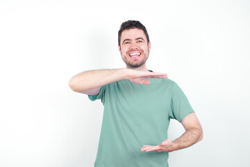 young handsome caucasian man wearing green t-shirt against white background gesturing with hands showing big and large size sign, measure symbol.