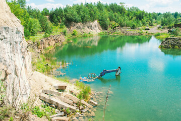 Old basalt quarry and sunken excavator. Summer landscape with lake and green fir forest in abandoned mining