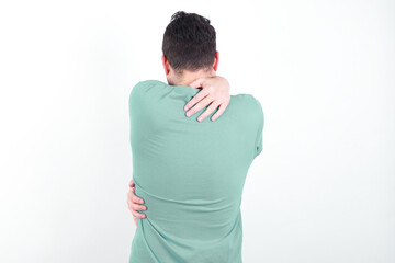 young handsome caucasian man wearing green t-shirt against white background hugging oneself happy...