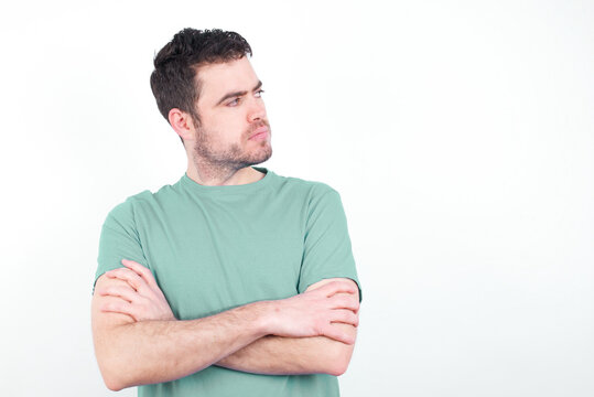 Image of upset young handsome caucasian man wearing green t-shirt against white background with arms crossed. Looking with disappointed expression aside after listening to bad news.
