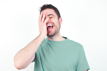 Charismatic carefree joyful young handsome caucasian man wearing green t-shirt against white background likes laugh out loud not hiding emotions giggling hear funny hilarious joke chuckling facepalm.