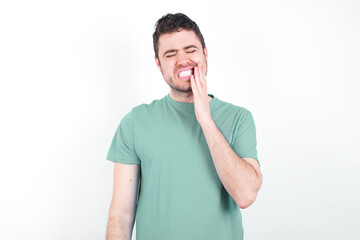 Tooth ache concept. Indoor shot of young handsome caucasian man wearing green t-shirt feeling pain,...