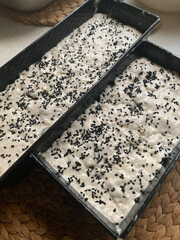 dough for bread risen and ready to be placed in the oven, oblong baking tins, seeds and cereals on bread from the mold, black cumin, sunflower seeds, leavened bread dough