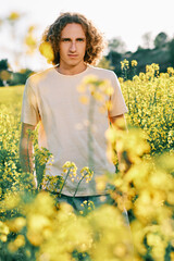 an stylish young man with curly hair with lots of flowers around him in a spring day