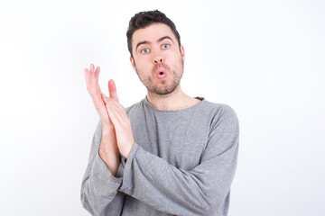 Surprised emotional young handsome caucasian bearded man wearing pyjama over white wall rubs palms and stares at camera with disbelief