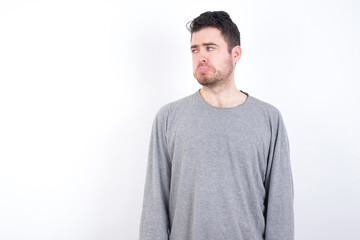 Fototapeta premium Dissatisfied young handsome caucasian bearded man wearing pyjama over white wall purses lips and has unhappy expression looks away stands offended. Depressed frustrated model.